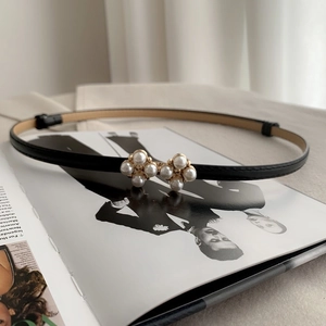 Detailed close-up of a black skinny leather belt with an elegant white pearl floral buckle