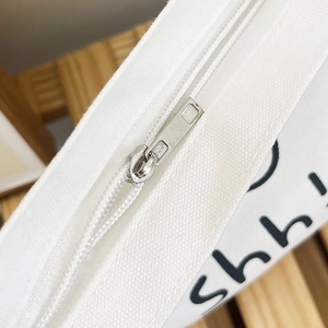 Detailed close-up of smooth silver metal zipper on white canvas crossbody handbag