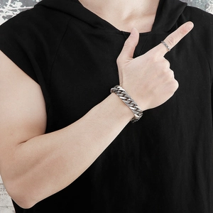 Close-up of a silver chunky Cuban link bracelet and slim ring on a male model's wrist