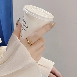 Detail of a minimalist gold hollow flower ring worn by a model holding a coffee cup