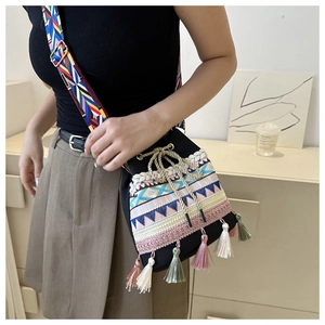Ethnic style black bucket bag with fringe detail and woven strap worn by a model