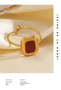 Detail of a square red enamel gold ring with textured band and a soft silk background