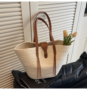 Detail of woven straw tote bag with brown leather straps and metallic buckle closure
