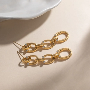 Détail de boucles d'oreilles maillons dorés avec anneaux ovales sertis de cristaux brillants