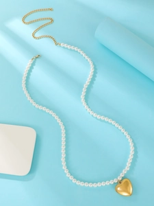 Macro shot of white pearl necklace with heart pendant and gold extender on blue surface