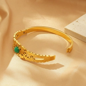 Vintage gold-plated evil eye bangle with green gemstone on champagne silk background