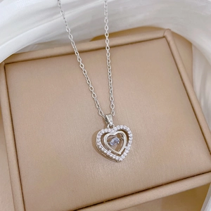 Close-up of a silver heart-shaped necklace with crystals on beige box and white silk
