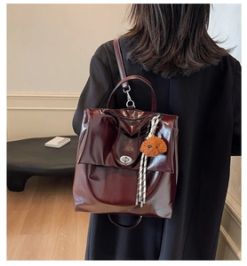 Detail of dark red glossy leather backpack with flip cover and cute brown bear pendant