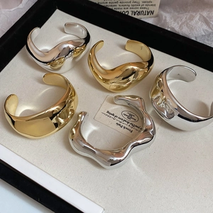 Dettaglio di bracciali rigidi irregolari in metallo fuso con finitura oro e argento