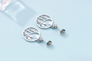 Detail view of silver cutout circular floral earrings in stainless steel on blue surface