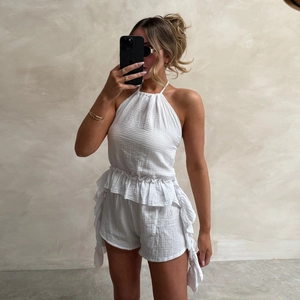 Detail of white halter neck romper in textured waffle fabric with ruffled hem finish