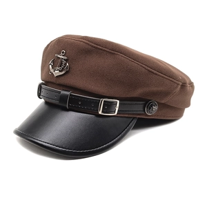 Detail of brown wool flat cap with black faux leather brim and metallic anchor badge
