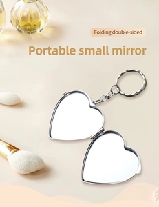 Macro detail of heart-shaped folding travel mirror with metal keychain on beige background