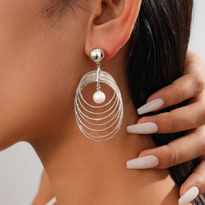 Close-up of multilayer silver circular earrings with pendant pearl on a female model