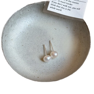 Minimalist freshwater pearl stud earrings with silver needles on a textured gray tray