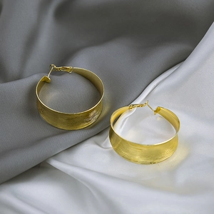 Macro shot of large golden C-shaped hoop earrings with a textured brushed metal surface
