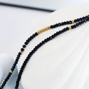 Handmade beaded necklace with black faceted beads and gold accents in a minimalist style