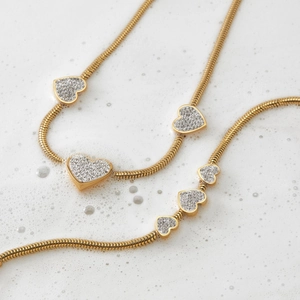 Gold heart pendant snake chain necklace set with sparkling crystals on white surface