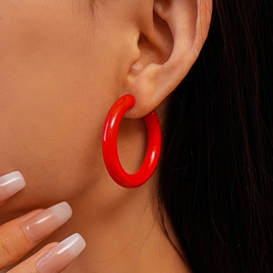 Gros plan d'un mannequin portant de grandes boucles d'oreilles créoles C rouge brillant