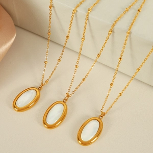 Gold beaded chain necklace with oval white shell pendant displayed on silk fabric background