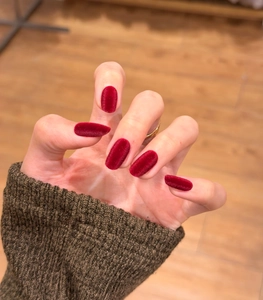 Detail view of burgundy velvet press-on nails with a matte flocking texture on hands