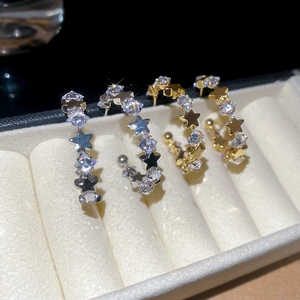 Close-up of gold and silver C-shaped earrings with sparkling star zircons on white velvet