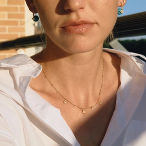 Gros plan d'un collier doré avec pendentifs éclair et cristal porté par une femme