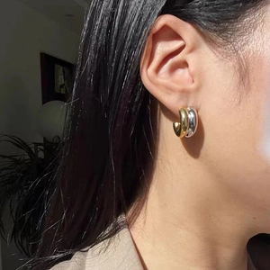 Polished 18K gold and silver two-tone C-shaped hoop earrings worn by a model