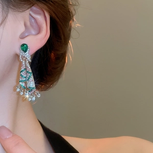 Close-up of dangling tassel earrings with emerald drop and shimmering crystal pendants