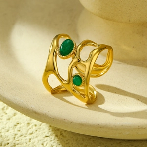 Detailed shot of hollow golden ring featuring two elegant green oval gemstones on ceramic