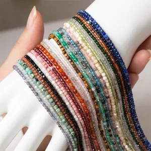 Hand holding assorted 2-3mm natural stone beads including amethyst and lapis lazuli strands