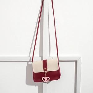 Detail of cream and burgundy crossbody bag featuring pink heart charms and slim strap