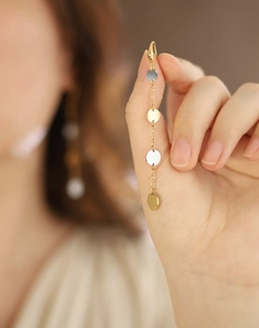 Detail of long drop earrings featuring two-tone silver and gold discs held by hand
