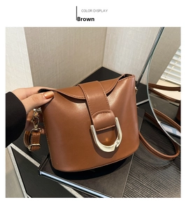 Close-up of brown bucket bag with gold U-shaped metal buckle and smooth faux leather