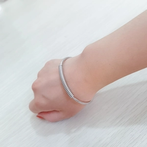 Detail of silver stainless steel spring cuff bracelet worn on wrist over wooden desk