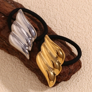 Detail of wing-shaped hair ties in gold and silver finish on a wooden surface