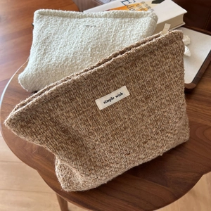 Close-up of textured wool cosmetic bags with zipper and simple wish label on a table