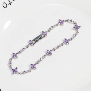 Close-up of a silver flower bracelet with purple zircon clovers on a ceramic plate