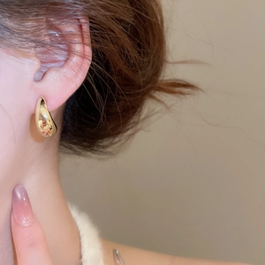 Close-up of minimalist gold teardrop earrings worn by a model in warm elegant lighting