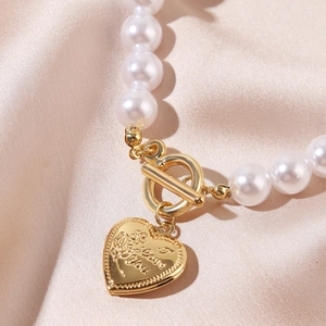 Detailed shot of baroque pearl necklace with gold heart Love You engraved charm and OT clasp