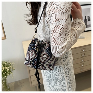Close-up of woven geometric pattern bucket bag with black faux leather strap on model
