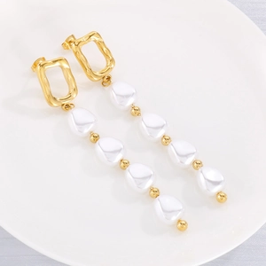 Détail de boucles d'oreilles dorées géométriques avec perles blanches sur plat blanc