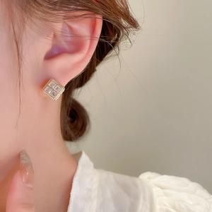 Close-up of square zircon earrings with gold plating on model's ear in warm light