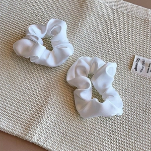 Close-up of two elegant white satin silk scrunchies on a soft woven texture surface