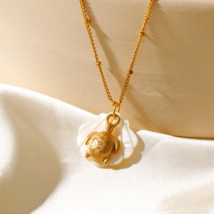 Détail du pendentif tortue dorée avec incrustation de nacre sur collier perlé