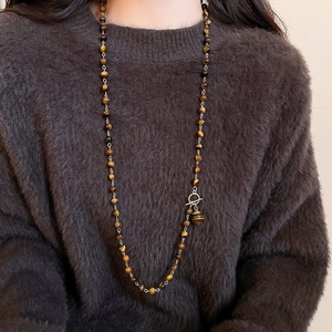 Dettaglio della collana vintage con occhio di tigre indossata su un maglione marrone