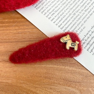 Close-up of a red plush hair clip with golden horse charm on a wooden desk background