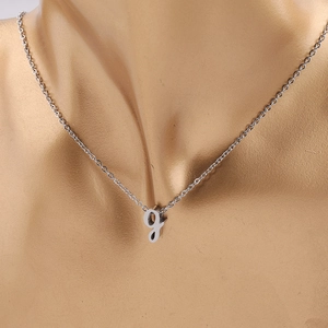 Gros plan du collier argenté avec pendentif lettre g minuscule en écriture cursive