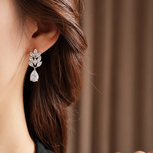 Macro detail of silver wheat leaf earring with pear-cut zircon on model's ear