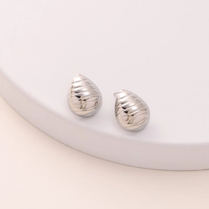 Minimalist silver water drop stud earrings with grooved stripe design on white stand